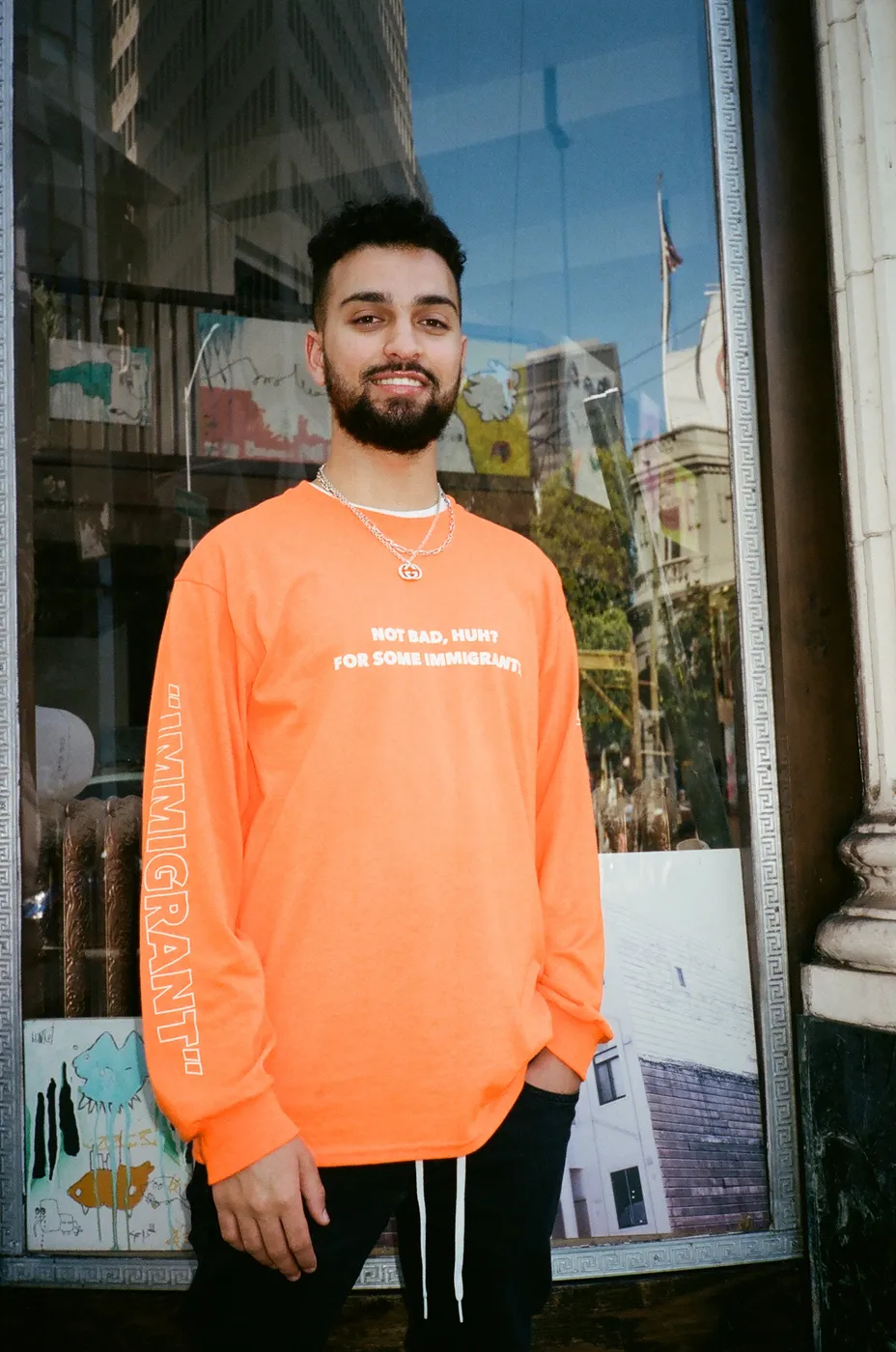 Model in the orange Not Bad, Huh? long sleeve in front of a storefront window